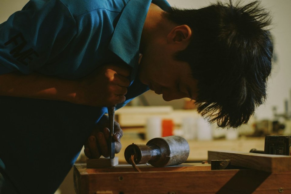 作業台に身を乗り出して、工具で部品を加工する人