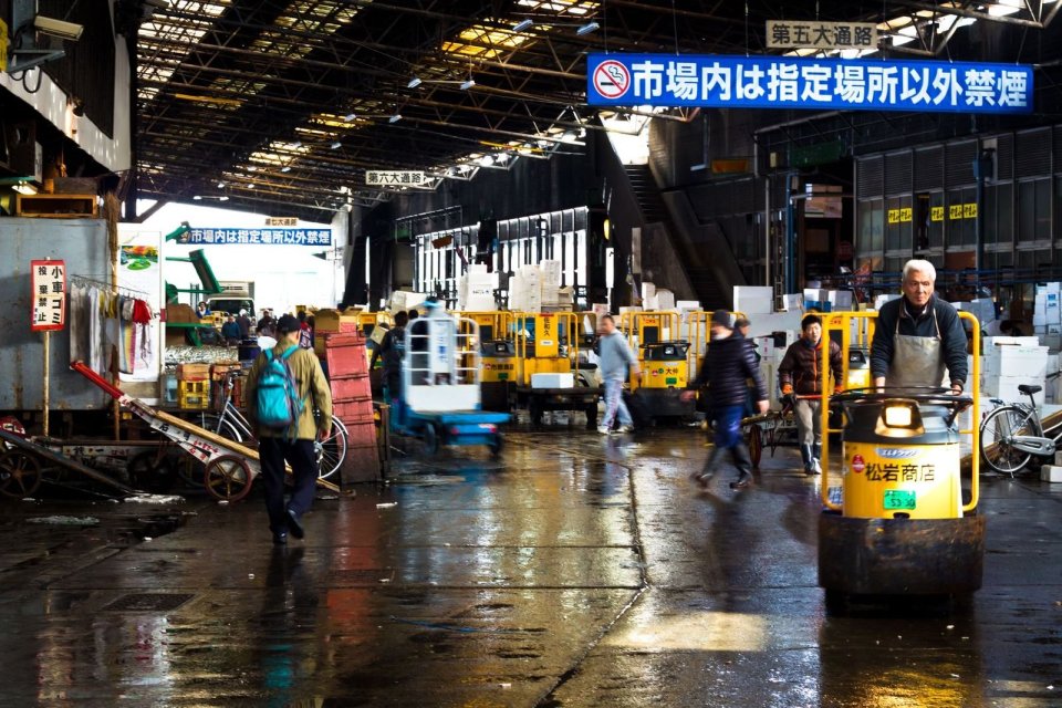市場の構内を、黄色い小型の運搬車で進む人と、行き交う人たち